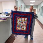 Two people holding up a quilt in a hospital room.