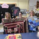 Three women holding up different types of quilts.