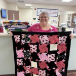A woman holding up a quilt in front of a counter.