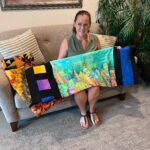 A woman sitting on top of a couch holding up two paintings.