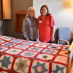 Two women standing next to a quilt on top of a bed.