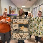 A group of women holding up some quilts